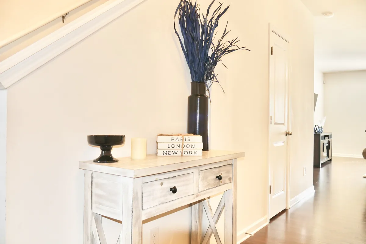 This image features a console table adorned with a blue decorative plant and travel-themed books, providing a welcoming entryway atmosphere. The scene conveys a cosmopolitan, inviting vibe, suggesting a sense of arrival and connection to new experiences.