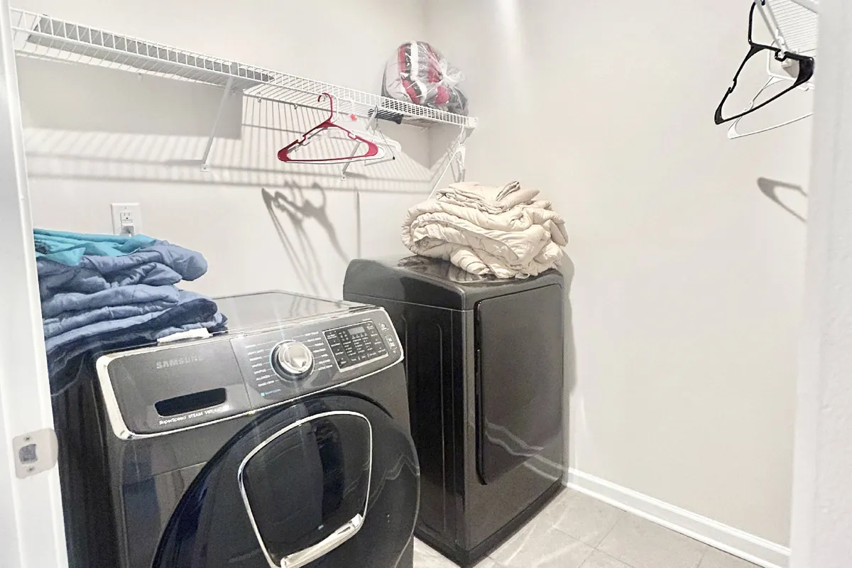 A well-organized laundry area is shown, featuring a washer, dryer, and shelves with neatly arranged clothes and cleaning supplies. The practical mood highlights convenience for longer stays.