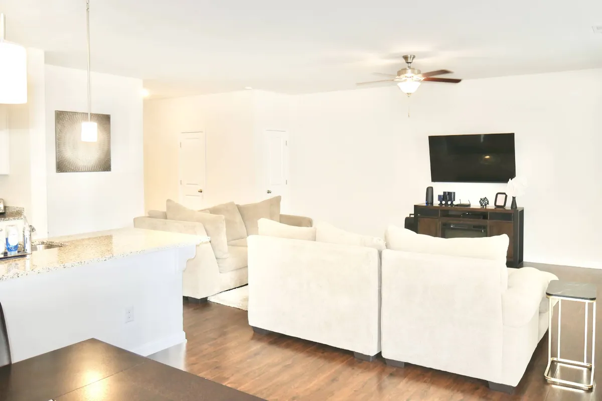 The image showcases the main living area with a comfortable sofa set, a television, a kitchen counter, and a dining table. The space is open and inviting, ideal for relaxation or family gatherings. Modern finishes and tidy organization suggest professional cleaning and thoughtful management.