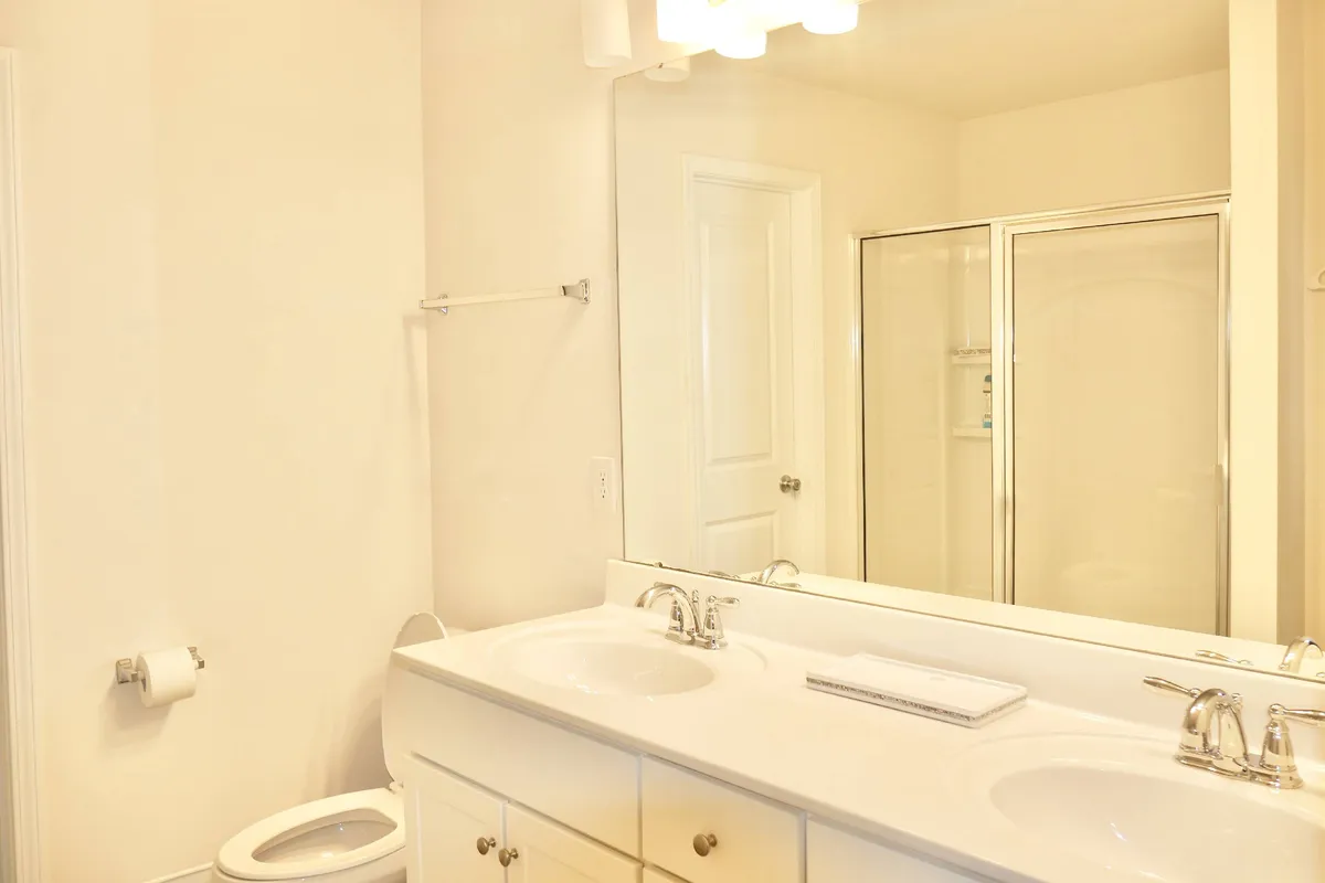A bright, spa-like bathroom with double sinks, a large mirror, and a walk-in shower. The space is flooded with morning light, emphasizing cleanliness and comfort for daily routines.