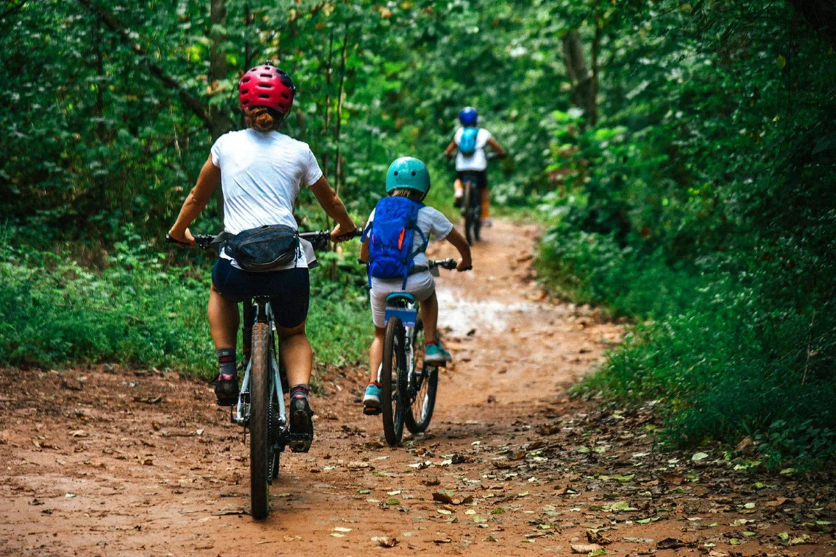 This image features a family biking along a lush, green dirt path surrounded by vibrant vegetation. The scene encapsulates the energetic spirit of outdoor adventure, with smiling faces and a sense of togetherness as the family explores nature.
