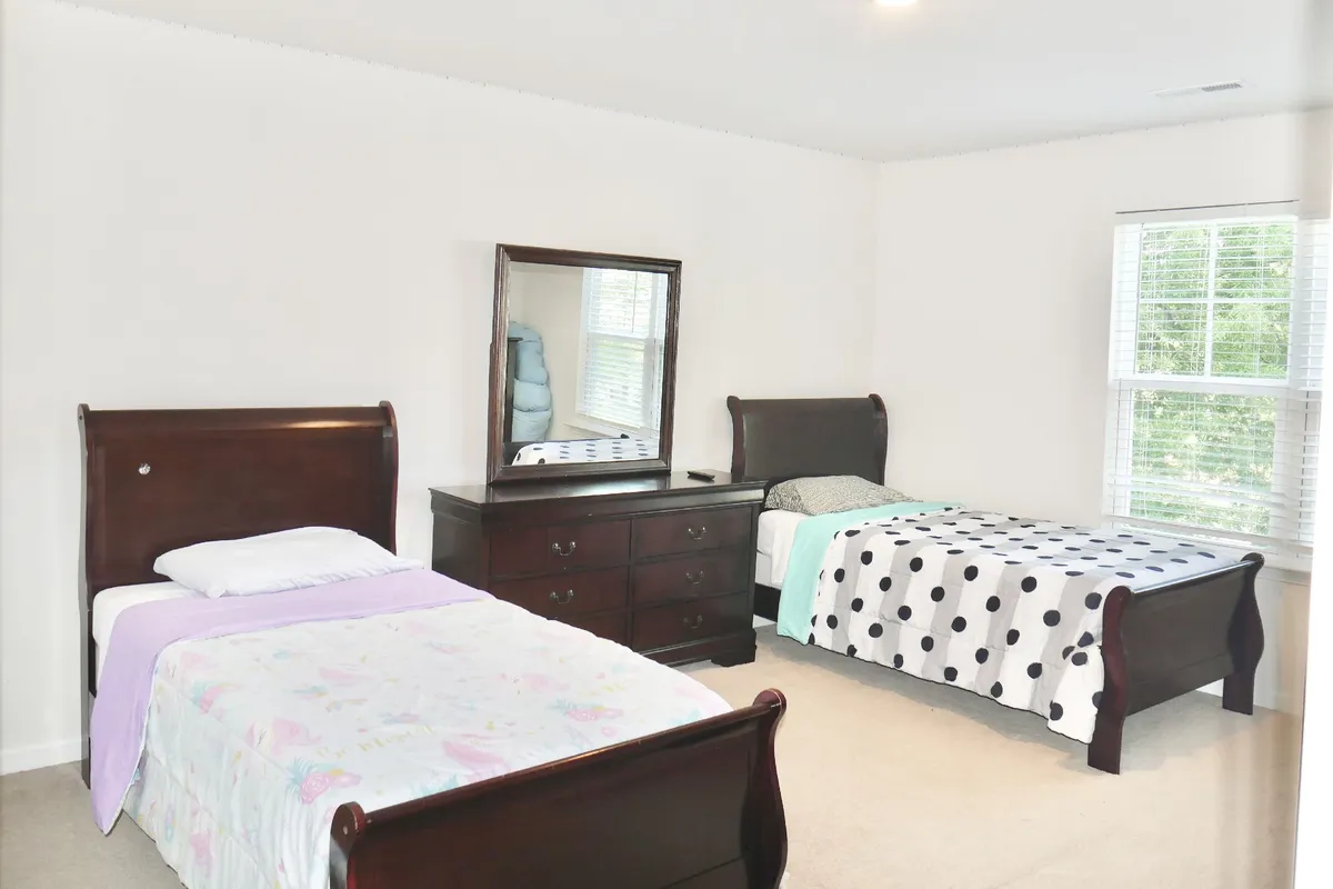 A cozy bedroom with two wooden beds, each dressed in playful polka dot and floral bedding. Sunlight streams in, giving the room a bright, welcoming feel. The arrangement hints at a shared space for friends or siblings, perfect for storytelling or winding down after a day of adventures.