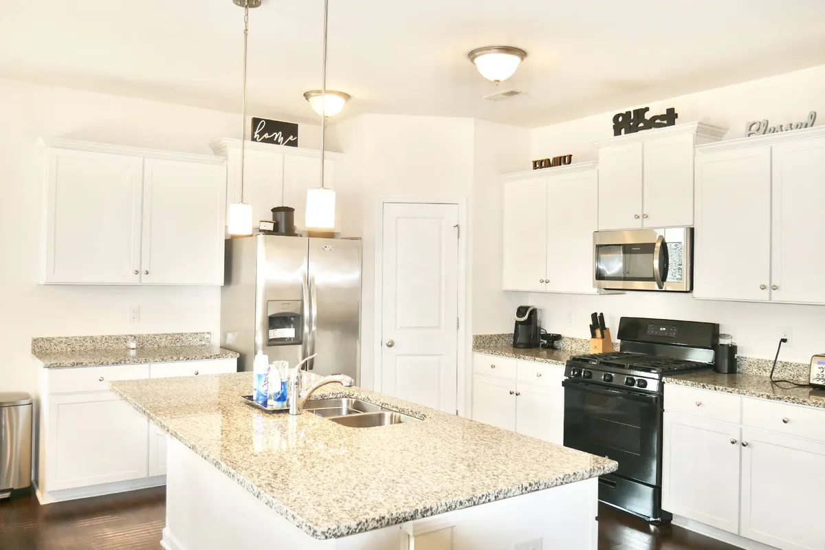 A bright kitchen scene with a granite countertop island, modern stainless steel appliances, and stylish light fixtures overhead. The set-up is ready for cooking, entertaining, and creating family traditions.
