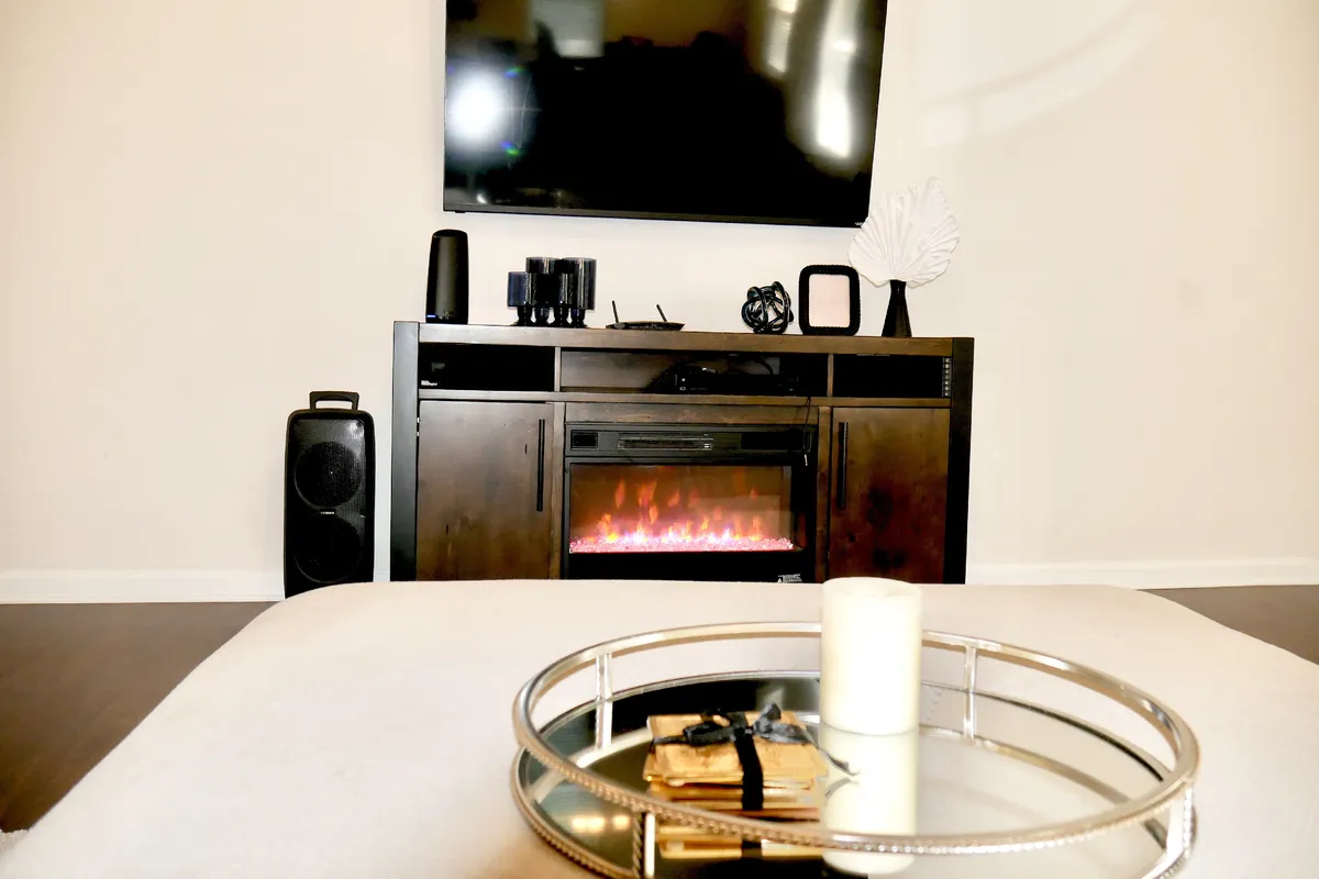 A warm, inviting living room scene centered around an elegant fireplace, with a smart TV above, a coffee table, and decorative accents. The setting is perfect for cozy nights by the fire or catching up with loved ones.